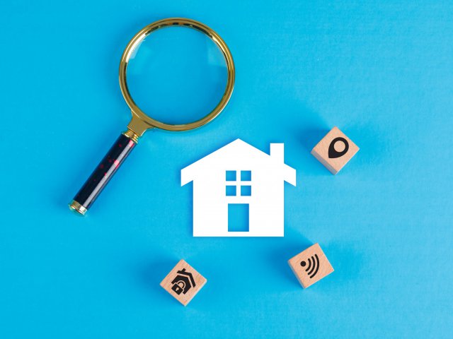 Conceptual of real estate with magnifying glass, wooden blocks, paper home icon on blue background flat lay. horizontal image